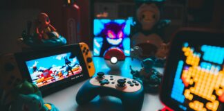 Como a regulação das apostas impacta a cultura gamer e eSports Mesa gamer com iluminação azul e vermelha reunindo um controle sem fio, console Nintendo Switch, miniaturas colecionáveis de Pokémon e uma Pokébola ao centro.